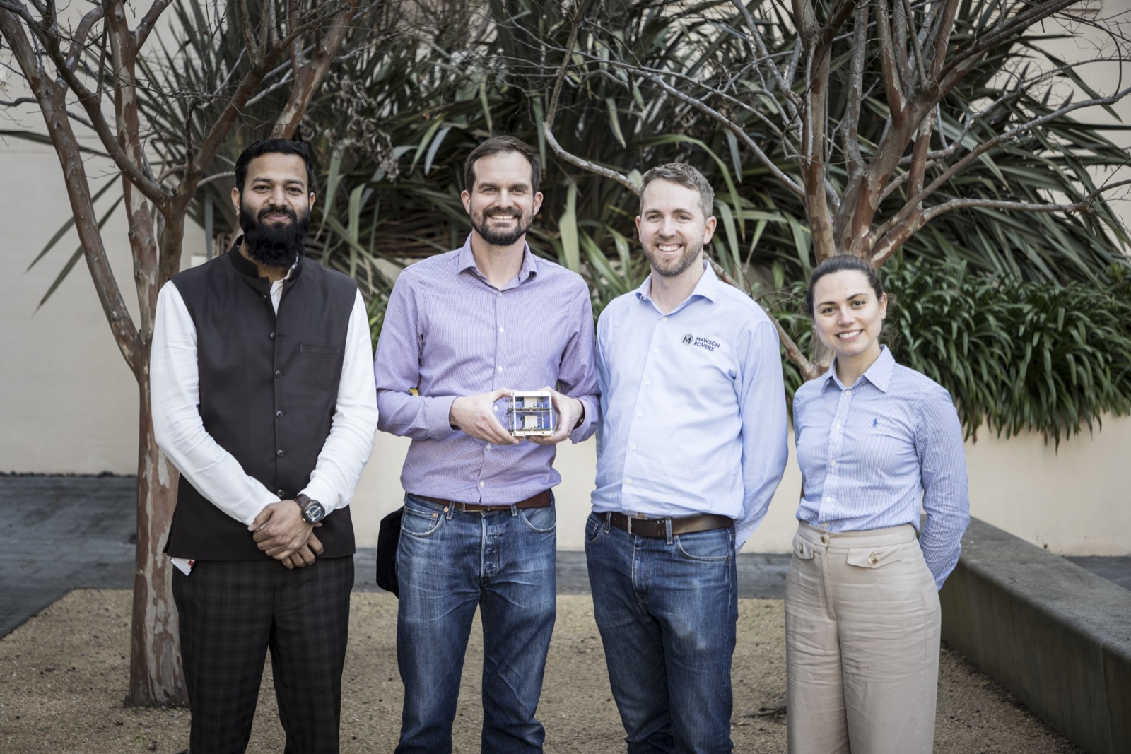 Four members of the UTS and Mawson Rovers team standing together outdoors,
             one of them holding the Matilda payload